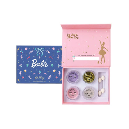A Barbie-themed mini makeup set shown with its blue outer box and the open pink inner kit. The kit contains four small cosmetic pots with face-painted lids, a gold glitter pan, and two dual-ended applicators.