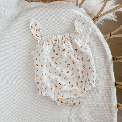 White baby romper with floral pattern on a textured surface