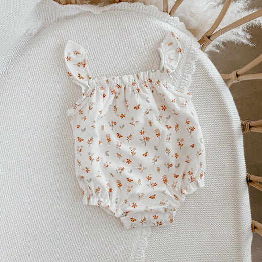 White baby romper with floral pattern on a textured surface