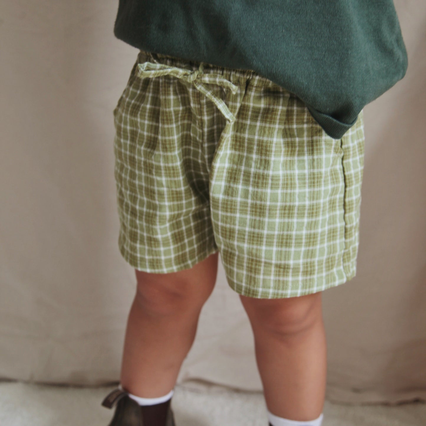Person wearing green plaid shorts and dark shoes on a neutral background
