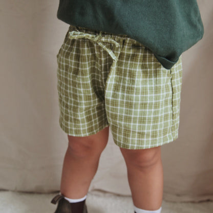 Person wearing green plaid shorts and dark shoes on a neutral background