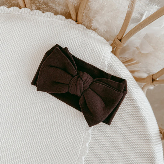 Brown headband with a bow on a textured white surface