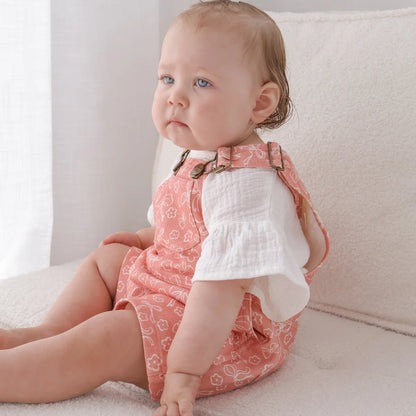Baby sitting on a couch wearing a pink patterned dress and white shirt.