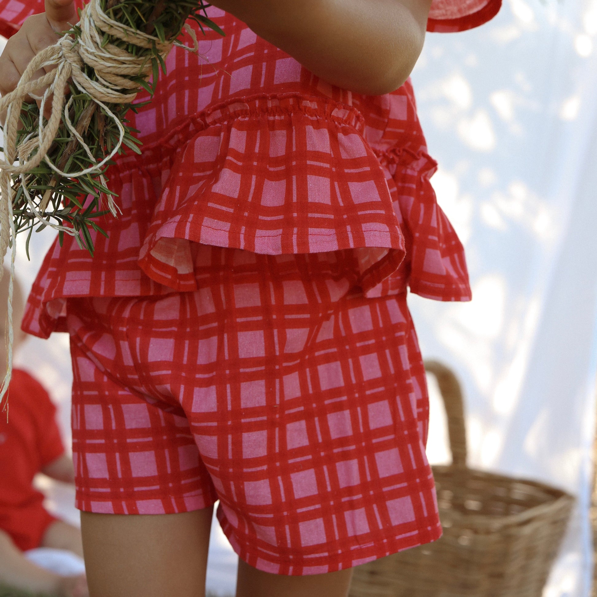 Child wearing a red and white checkered outfit holding a bundle of greenery.