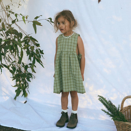 Young girl in a green checkered dress standing in a snowy landscape with trees and a basket.