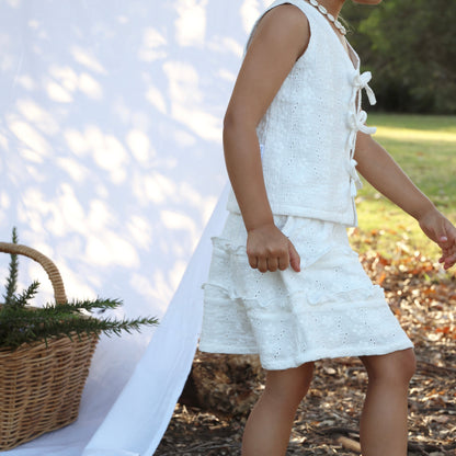 Young girl in a white dress standing outdoors with a basket and white fabric.