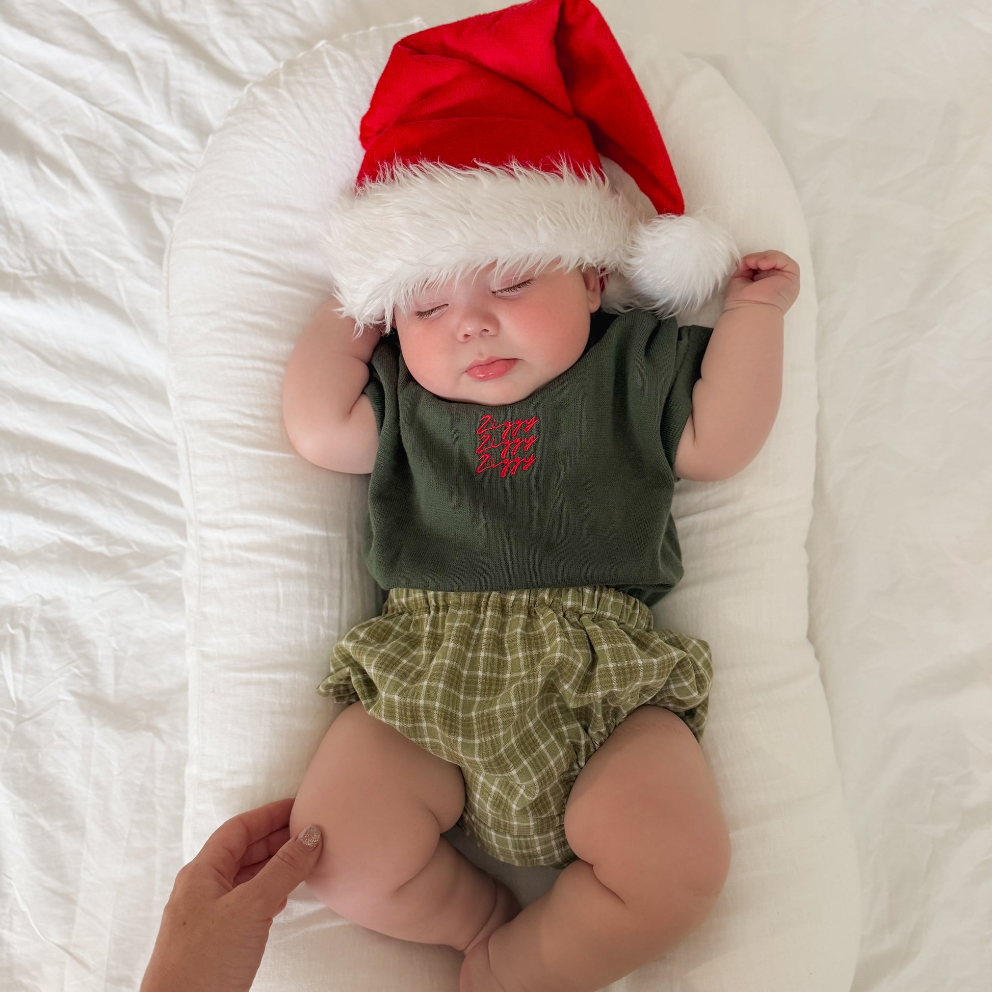 Baby wearing a Santa hat and green outfit lying on a white surface