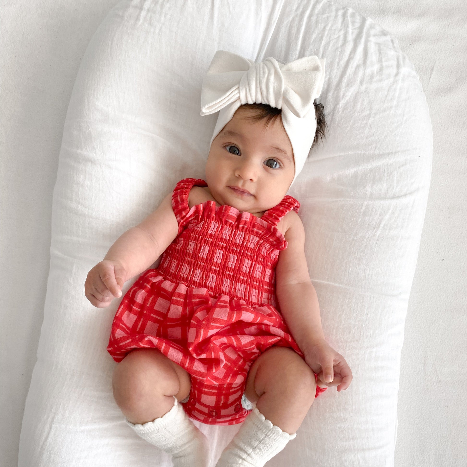 Baby in a red checkered outfit with a white bow on a white background