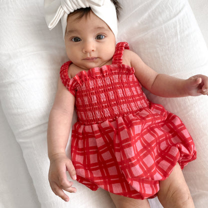 Baby wearing a red checkered outfit and white headband on a white background