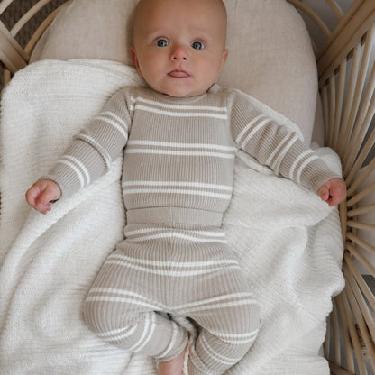 Baby in a striped outfit lying on a white blanket in a wicker crib.