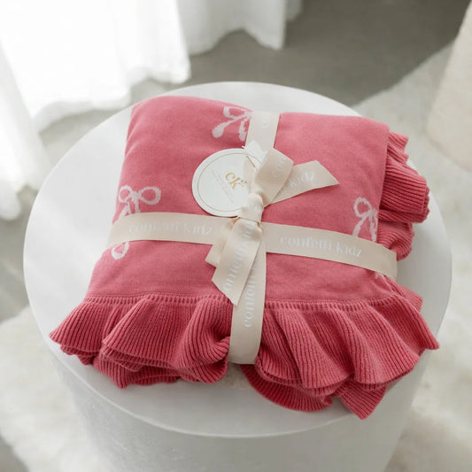 Pink baby blanket with ruffles on a white stool