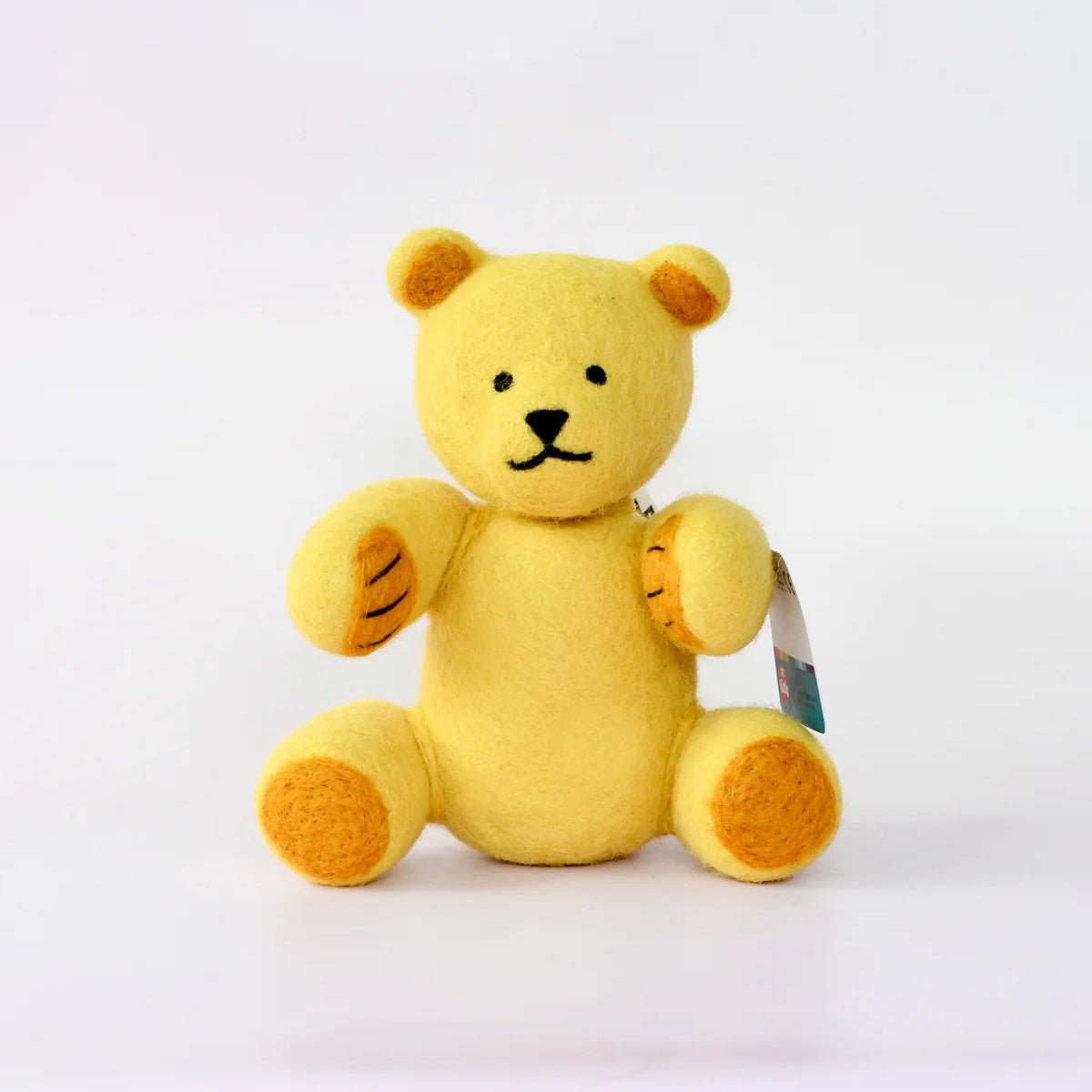 A small yellow plush teddy bear with embroidered black facial features and orange-brown paw pads, sitting against a plain white background with a small hangtag attached.