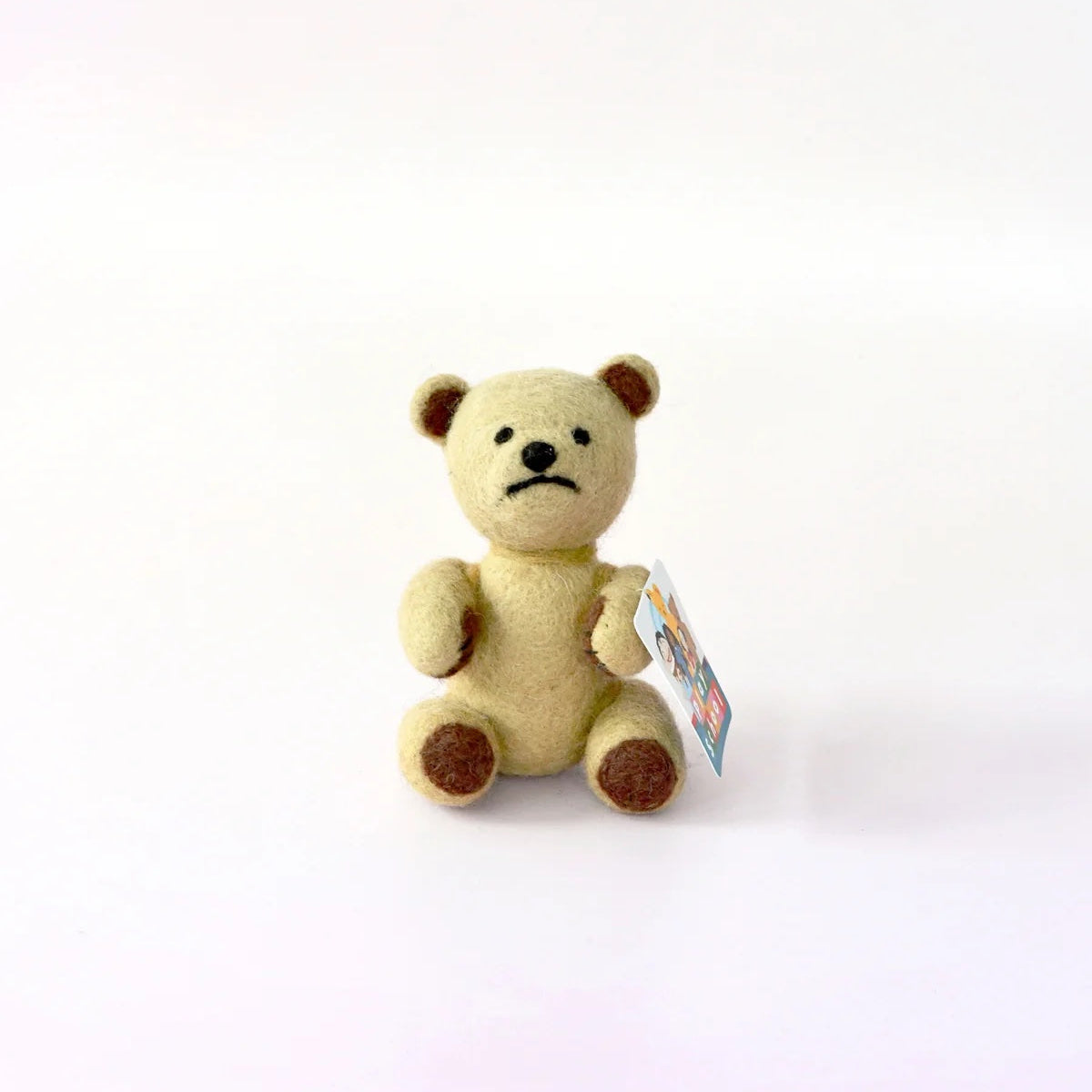 Small beige teddy bear with a tag on a white background
