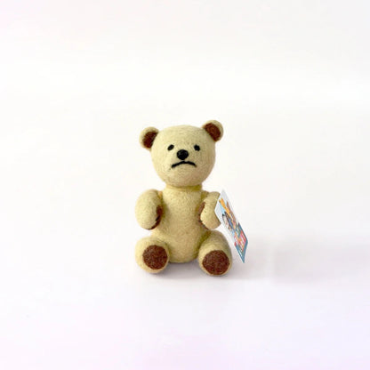 Small beige teddy bear with a tag on a white background