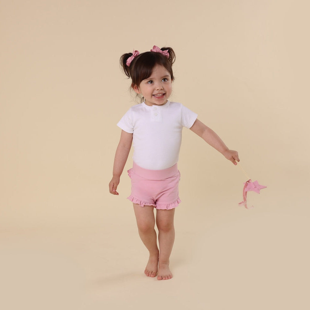 Young girl in a white shirt and pink shorts standing on a beige background