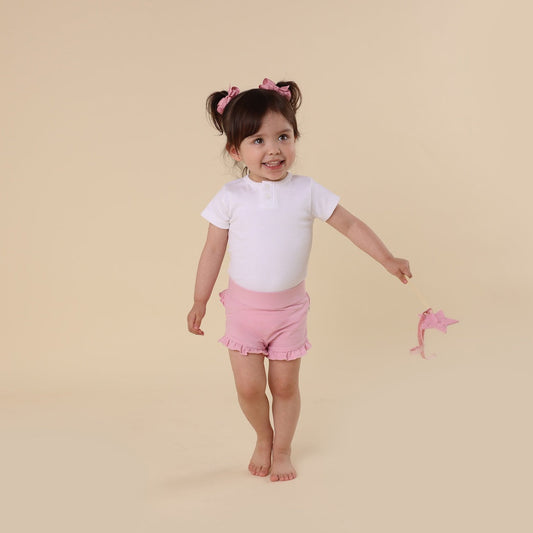 Young girl in a white shirt and pink shorts standing on a beige background