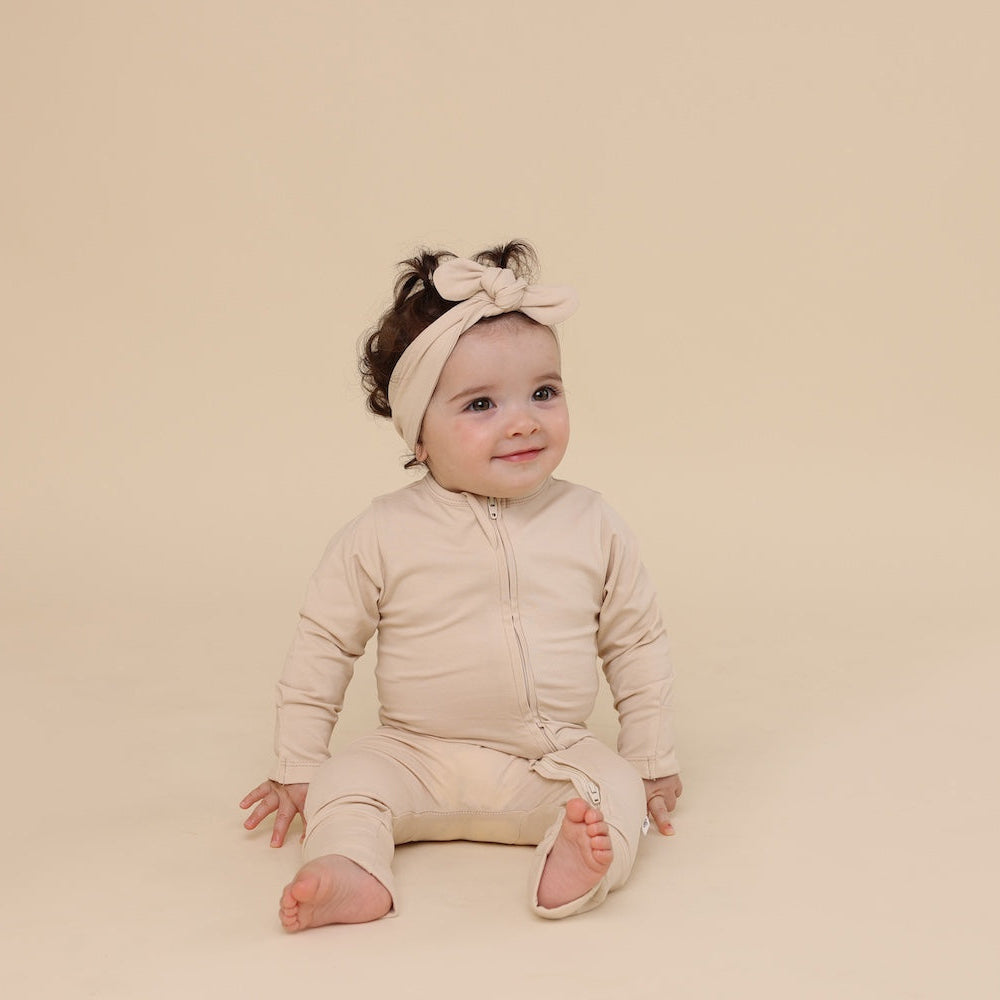 Baby in a beige outfit with a headband sitting on a beige background
