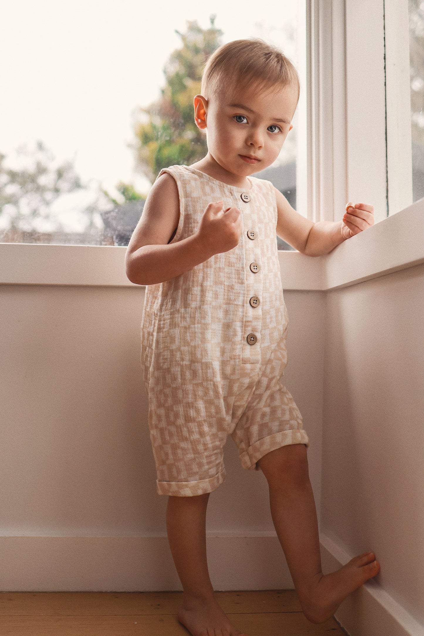 Child wearing a patterned romper standing by a window