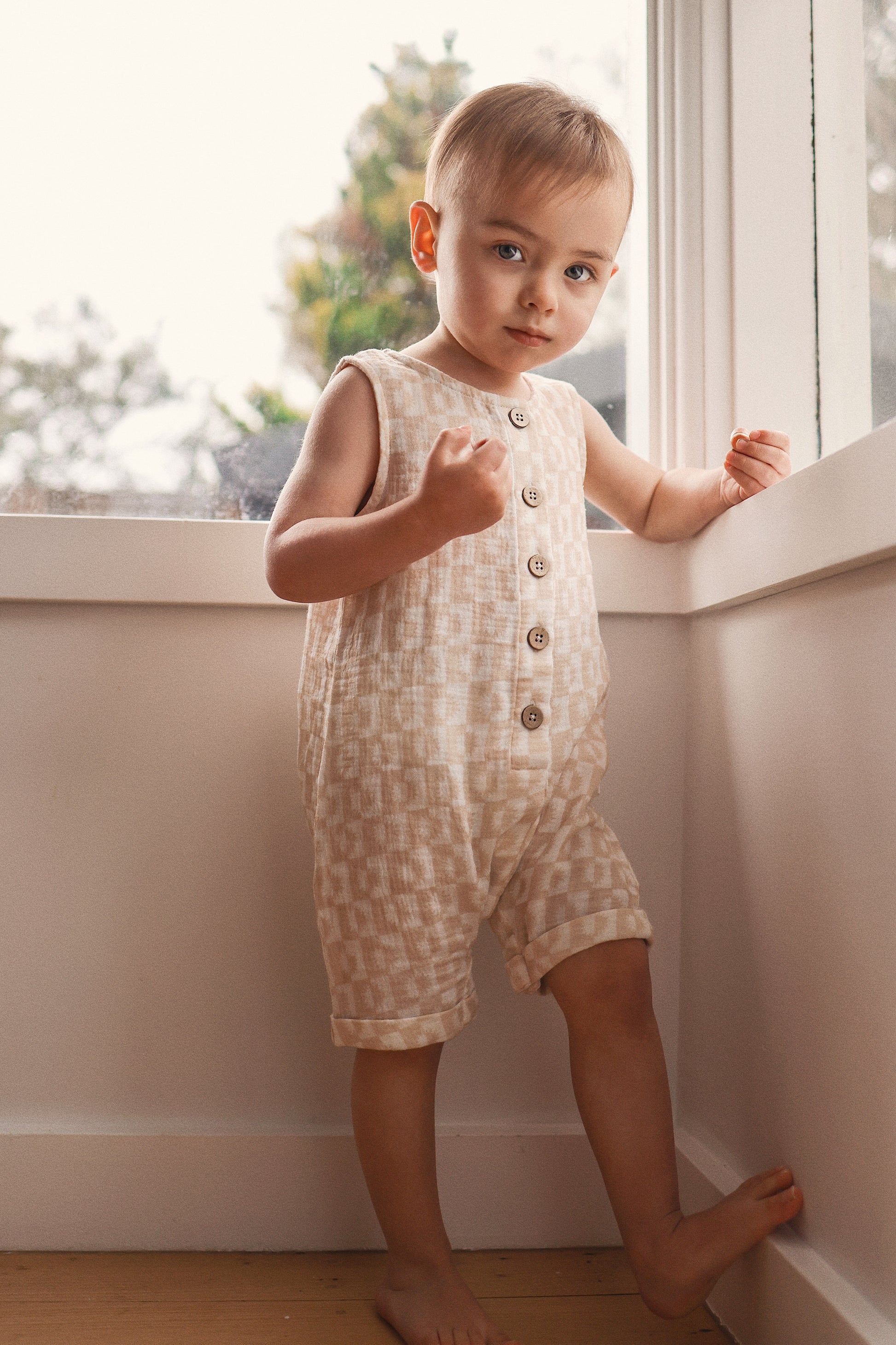 Child wearing a patterned romper standing by a window
