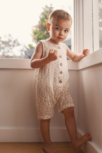 Child wearing a patterned romper standing by a window