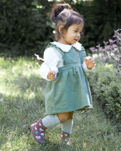 Young girl in a green dress standing in a grassy field with flowers.