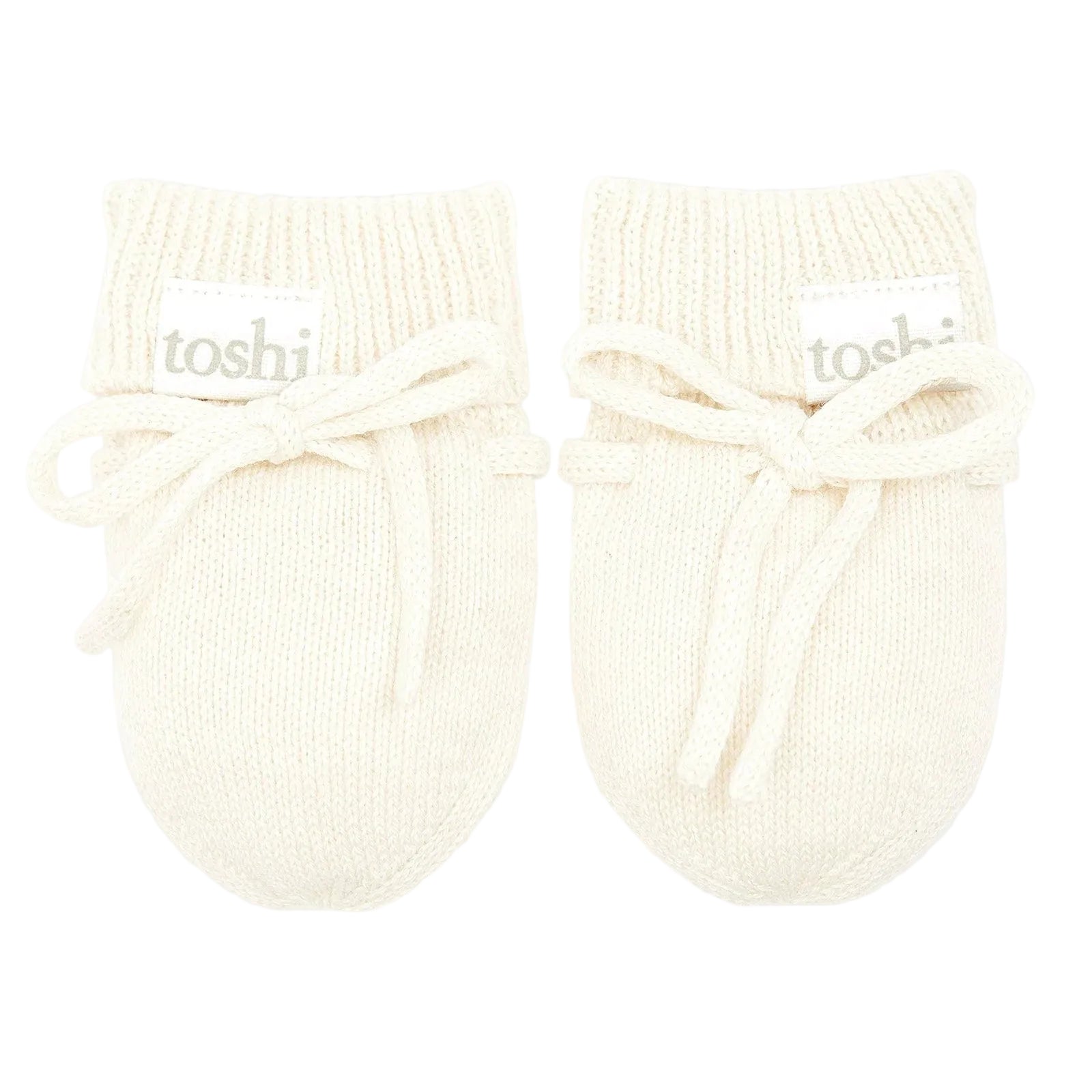 Pair of cream-colored baby booties with 'toshi' branding on a light gray background