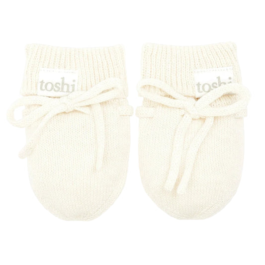 Pair of cream-colored baby booties with 'toshi' branding on a light gray background