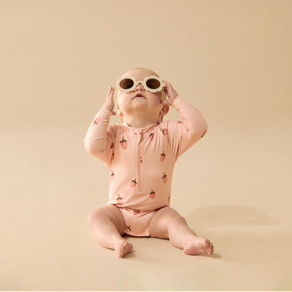 Baby wearing a pink strawberry-patterned onesie and sunglasses on a beige background