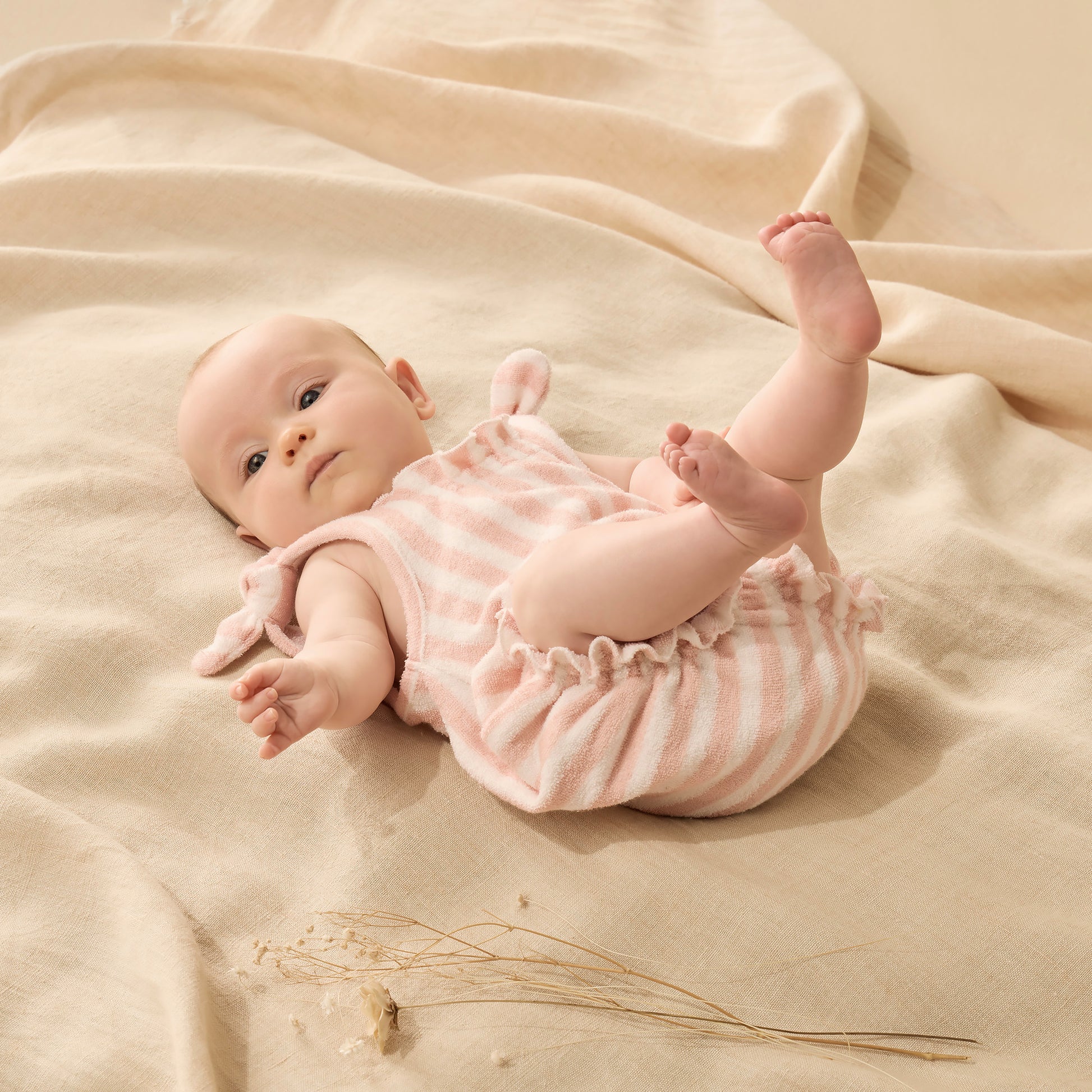Baby lying on a beige blanket wearing a pink and white striped outfit.