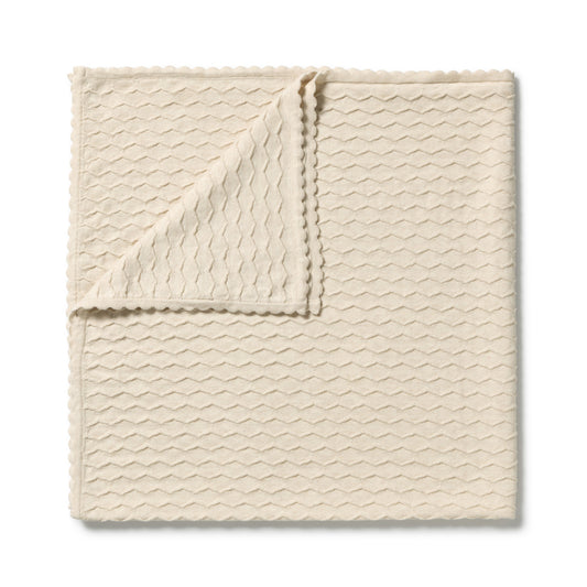 A folded cream-colored textured cloth with a wavy pattern and scalloped edges, displayed on a clean white background.
