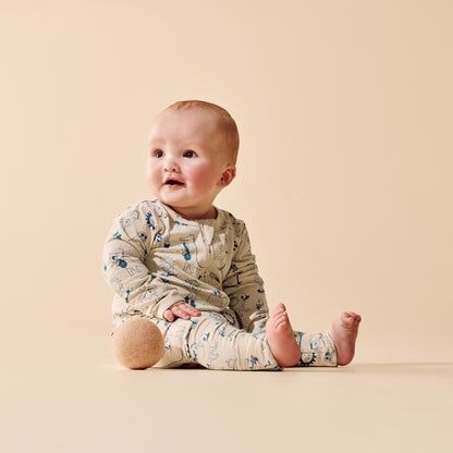 A baby sitting on a warm beige studio background, wearing a long-sleeve cream-colored romper with a blue and brown animal print.