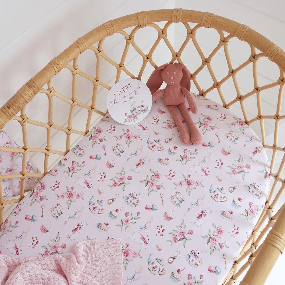 Floral-patterned crib sheet on a wicker crib with a soft toy and pink blanket.
