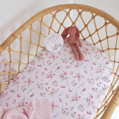Floral-patterned crib sheet on a wicker crib with a soft toy and pink blanket.