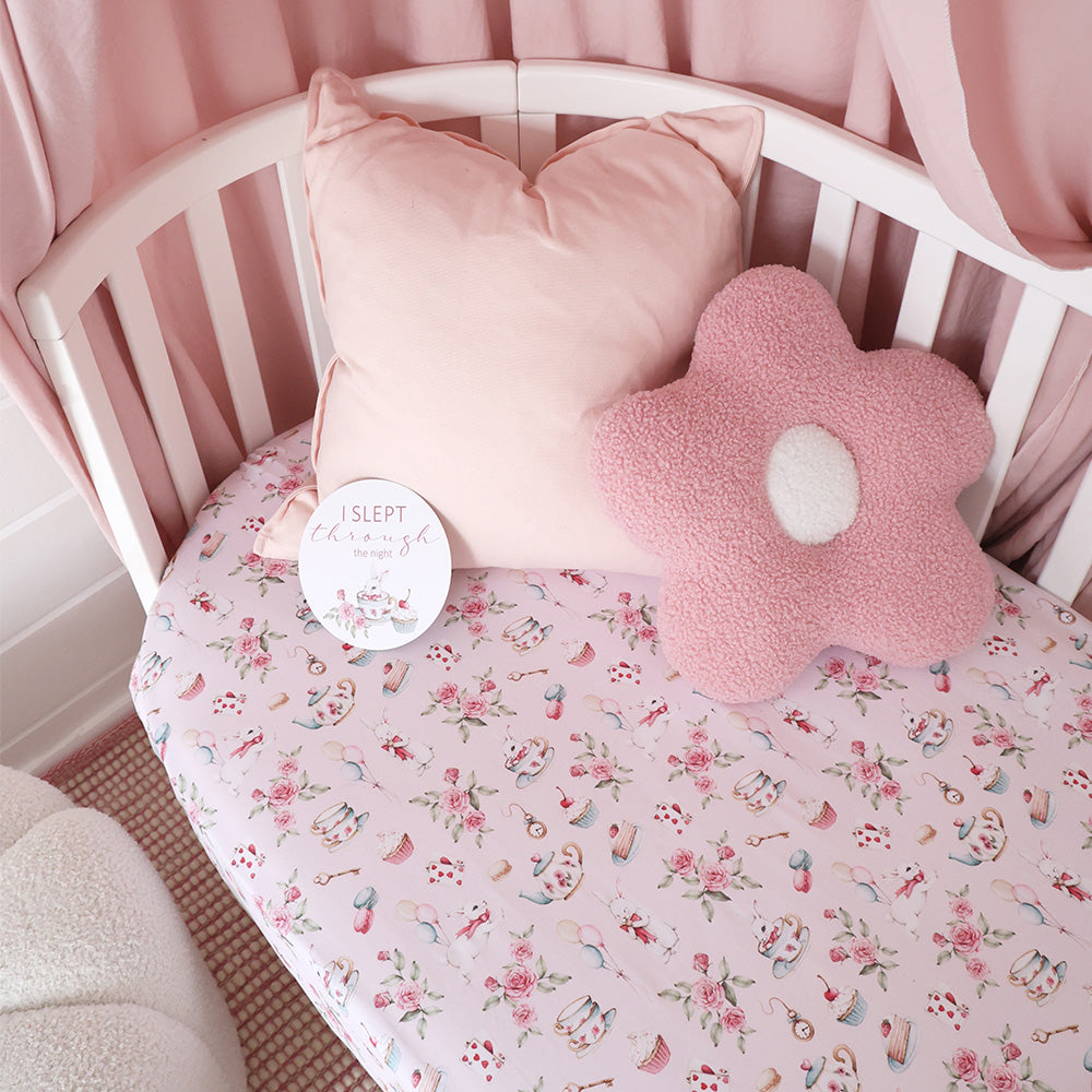 Crib with pink floral bedding, pillow, and flower-shaped cushion.
