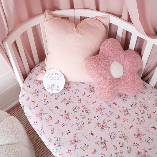 Crib with pink floral bedding, pillow, and flower-shaped cushion.