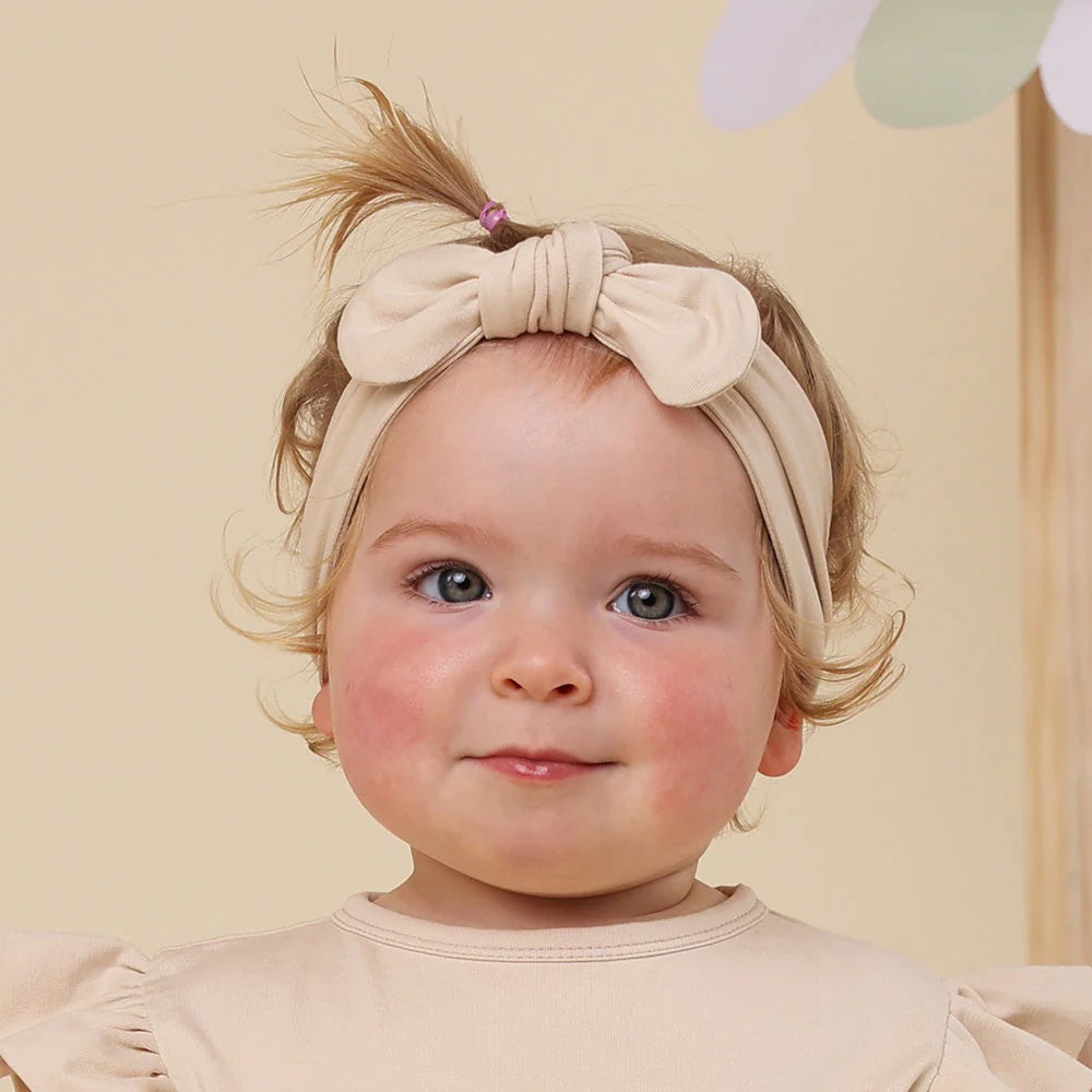 Baby wearing a beige headband with a bow against a light background