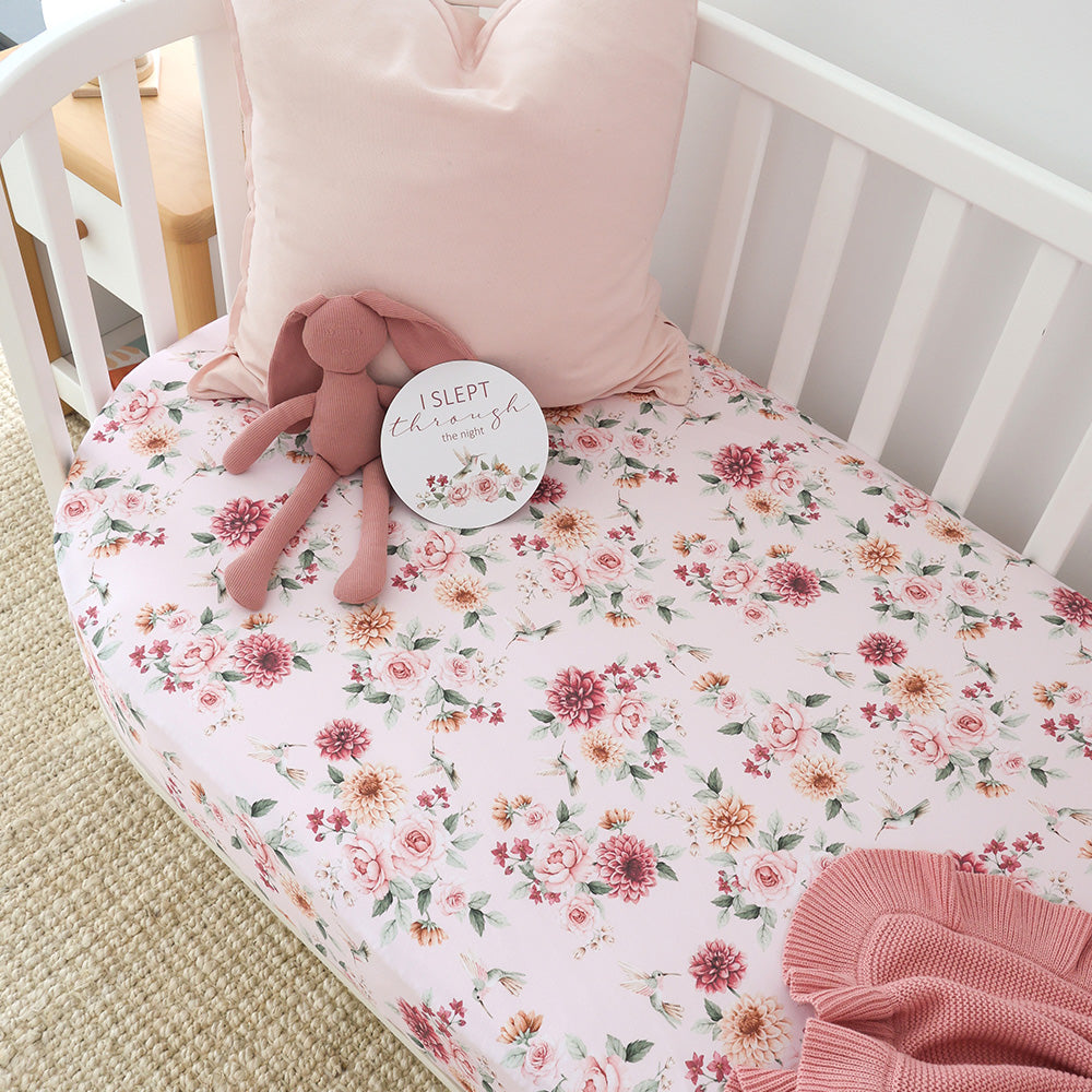 Floral crib sheet with a pink plush toy and a round tag on a crib.