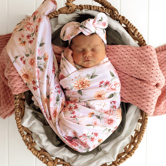 Newborn baby wrapped in a floral swaddle with matching headband in a wicker basket.