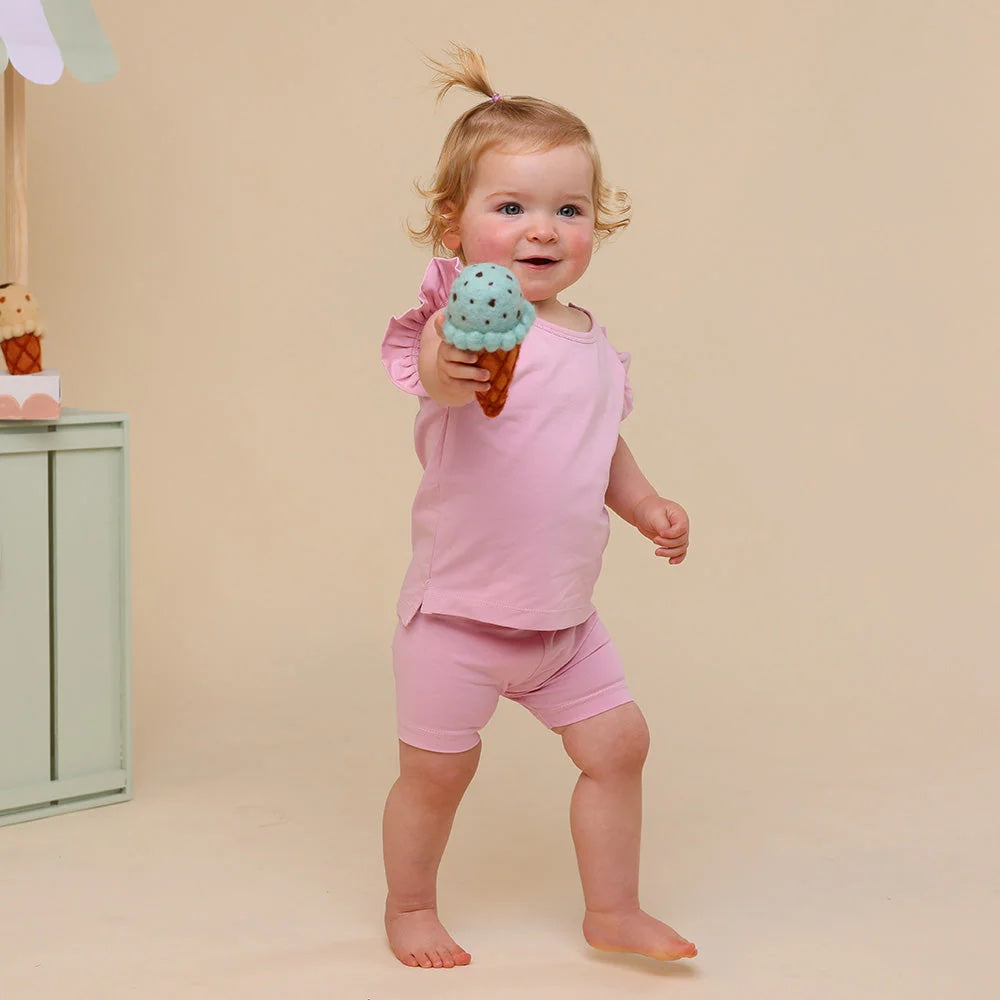 Child in pink outfit holding a toy ice cream cone against a beige background