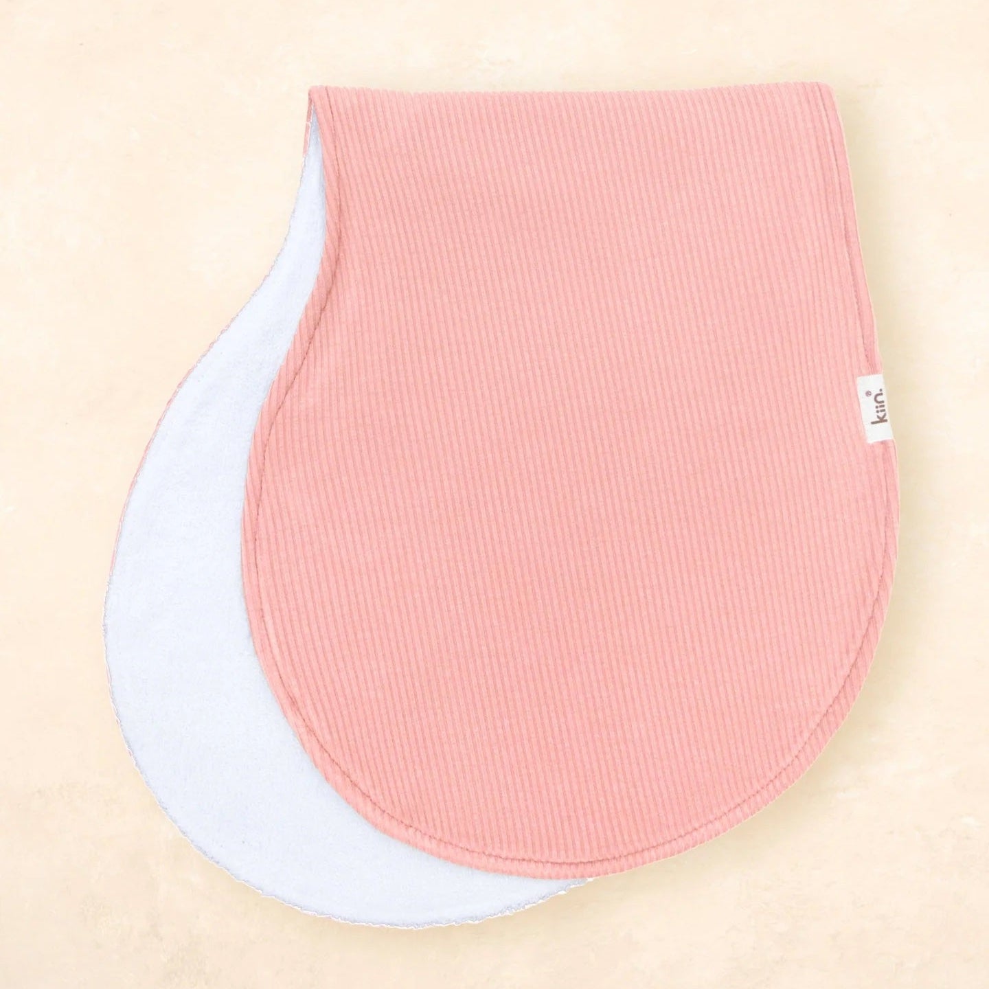 Two baby bibs, one pink and one white, on a beige background