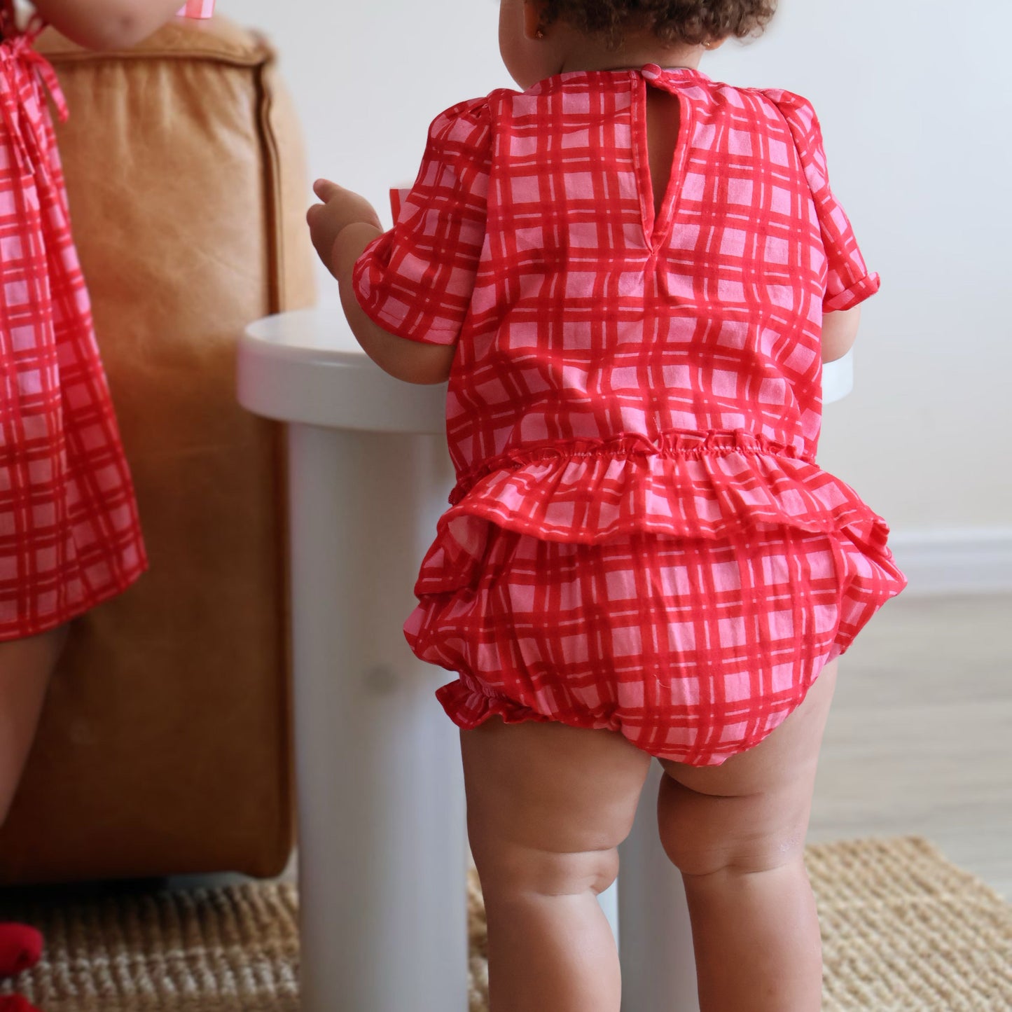 Child wearing a red checkered outfit standing in a room with a white sink.
