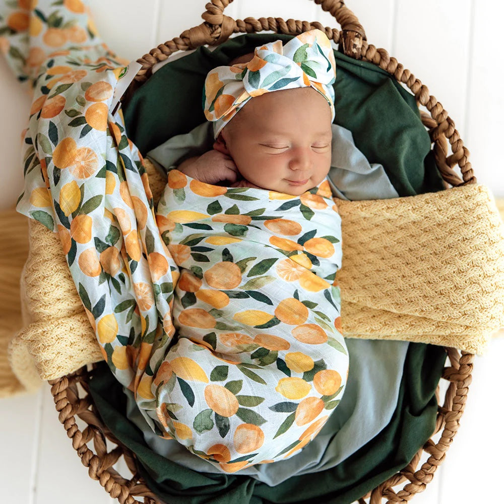 Newborn baby wrapped in a floral swaddle blanket and wearing a matching headband, lying in a woven basket.