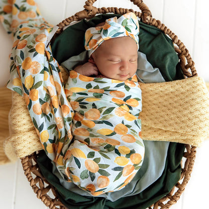 Newborn baby wrapped in a floral swaddle blanket and wearing a matching headband, lying in a woven basket.