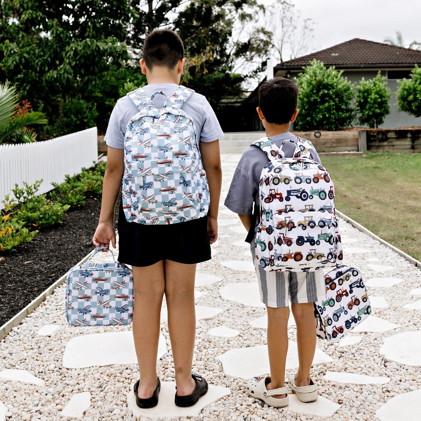 Two children with patterned backpacks walking on a stone path outdoors.