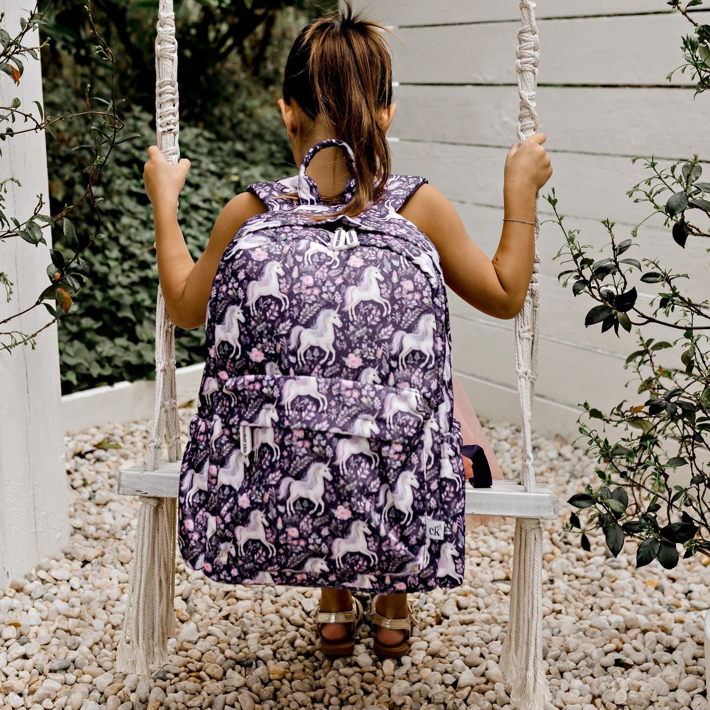 Person wearing a purple backpack with white patterns on a swing