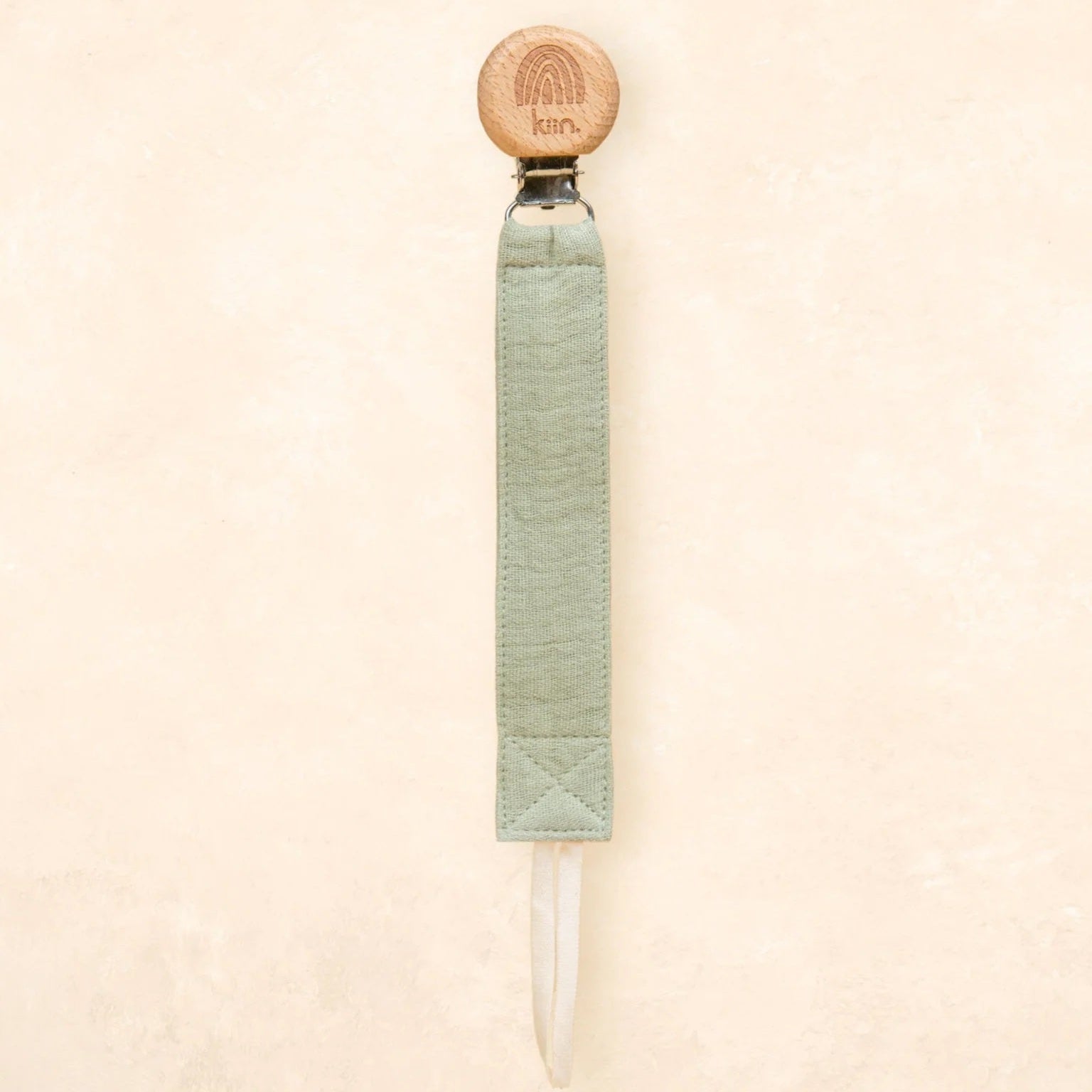 A single product shown against a plain textured beige background. The product is a long, narrow tool with a round light wood top, a pale sage green wrapped handle, and a clear pointed tip extending from the bottom.