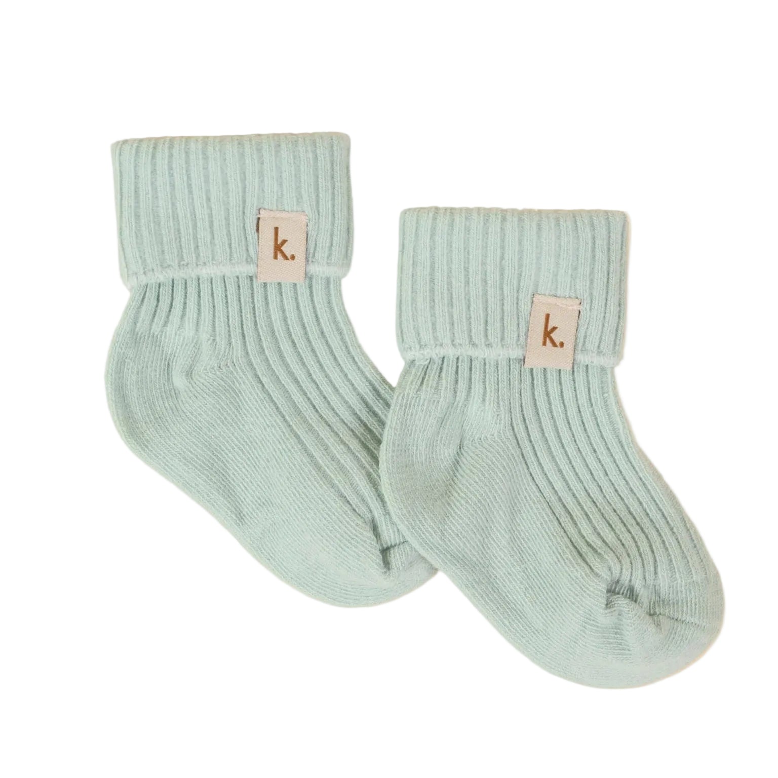 A pair of light mint green ribbed knit baby socks with a small beige leather patch featuring the lowercase 'k' logo, displayed on a textured cream background.