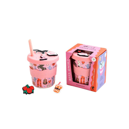 Pink tumbler with straw and decorative elements next to its packaging on a white background