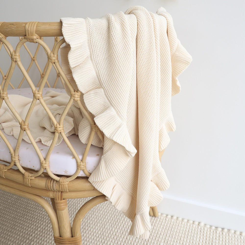 Beige knitted blanket draped over a wicker chair against a white wall.