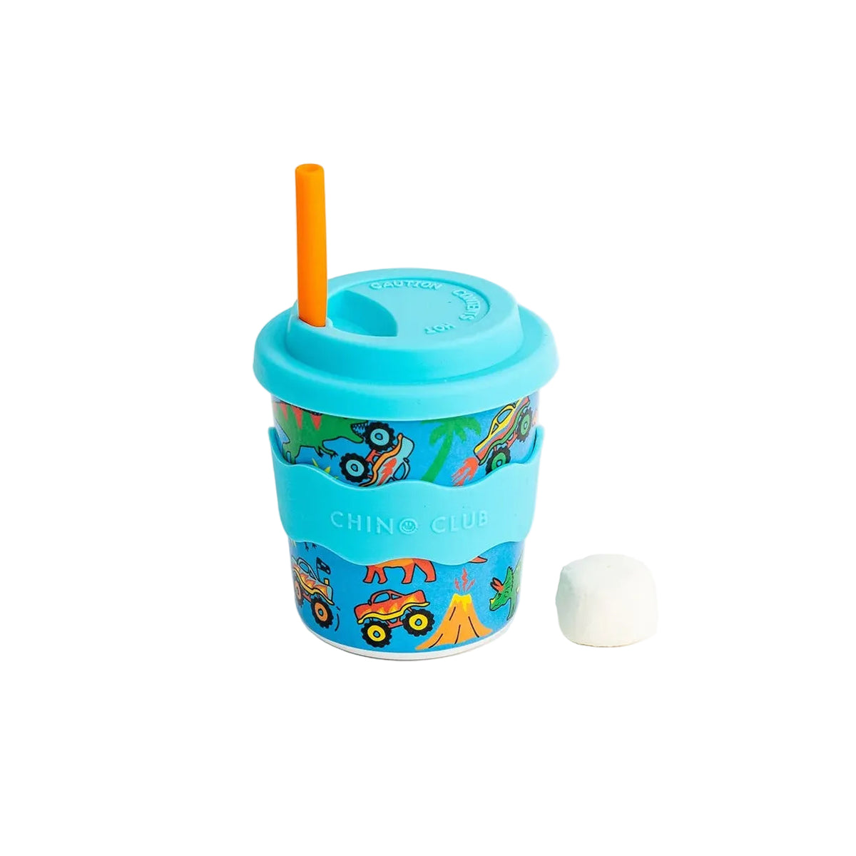 A small reusable travel tumbler with a bright blue lid and matching blue silicone sleeve, decorated with colorful cartoon construction vehicles and yellow-orange mountains. An orange straw sticks out of the lid, and a small white marshmallow sits beside it on a clean white background.